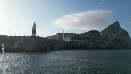 A low flying drone shot flying towards cliffs at the southernest point of Gibraltar below its red and white lighthouse.