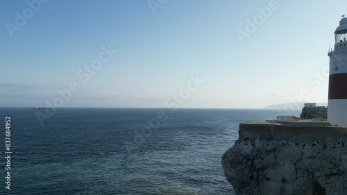 4K drone shot rising up over the ocean and panning to the right to reveal the rock of Gibraltar and its lighthouse at sunset.