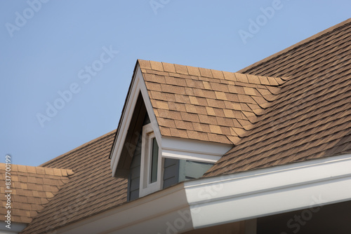 Roof shingles with garret house on top of the house. dark brown asphalt tiles on the roof background with blue sky.