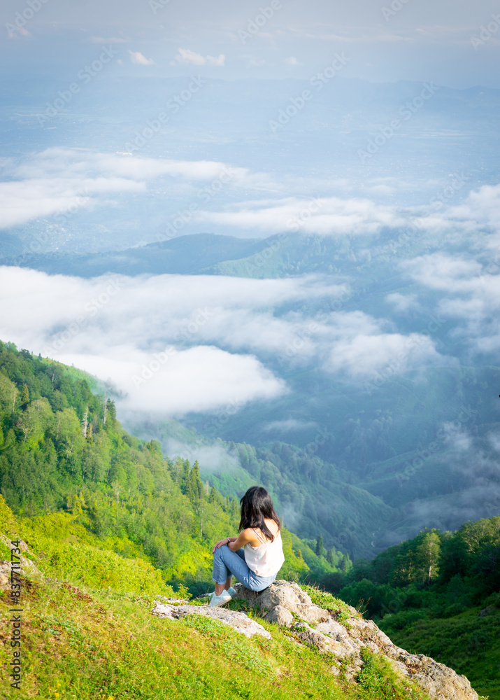 Naklejka premium Woman sits in nature above the clouds and enjoy nature panorama. Georgia travel pristine nature