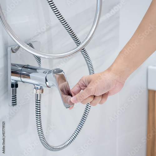 Male hand closing chrome shower water tap in white modern bathroom. Saving water concept photo