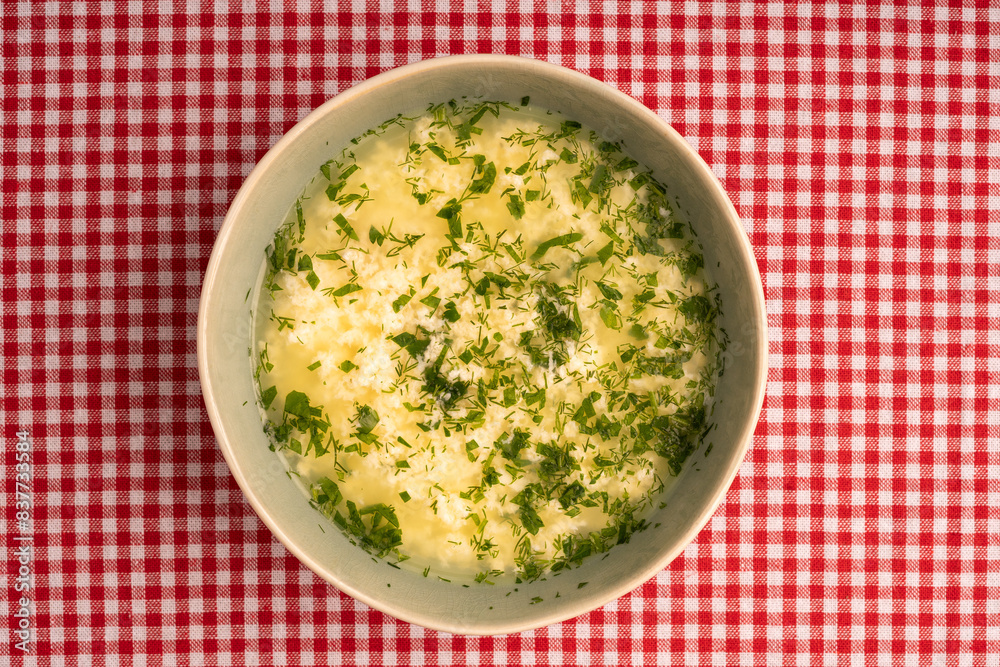 Italian stracciatella egg drop soup with parsley in bowl on tablecloth background, top view. Italian stracciatella egg drop soup with parsley in bowl on tablecloth background, top view.