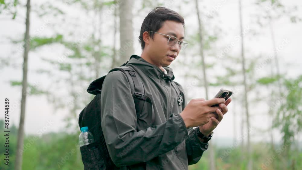 Male hiker in hiking clothes with backpack surveying a route on a map with phone in hand. Take a break during the trip Man looking at map on smartphone. Hiking in the forest.