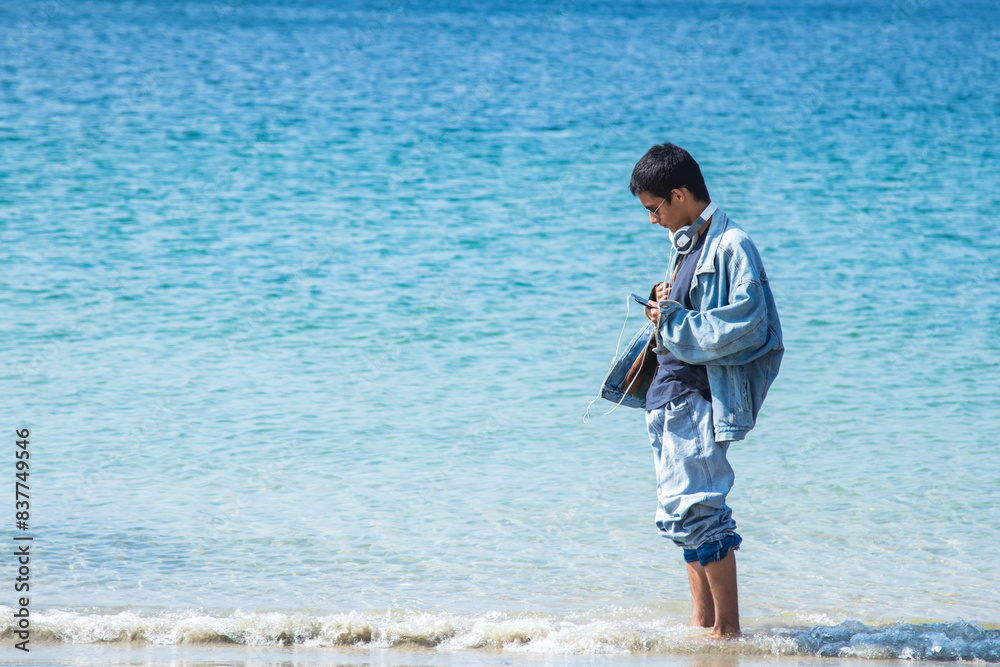 young man with headphones and phone relaxed walking on the beach young man with headphones and phone relaxed walking on the beach