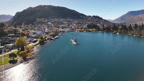 Relaxing drone view of steamboat leaving Queenstown, resort town on lakeshore. Sunny day in New Zealand. photo