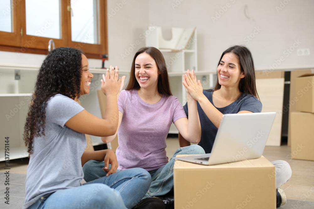 Three happy roommates moving home celebrating giving five Three happy roommates moving home celebrating giving five