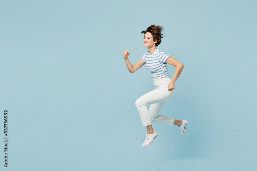 Full body side view fun young woman wears striped t-shirt casual clothes jump high run fast hurry up be in rush isolated on plain pastel light blue cyan background studio portrait. Lifestyle concept. Full body side view fun young woman wears striped t-shirt casual clothes jump high run fast hurry up be in rush isolated on plain pastel light blue cyan background studio portrait. Lifestyle concept.