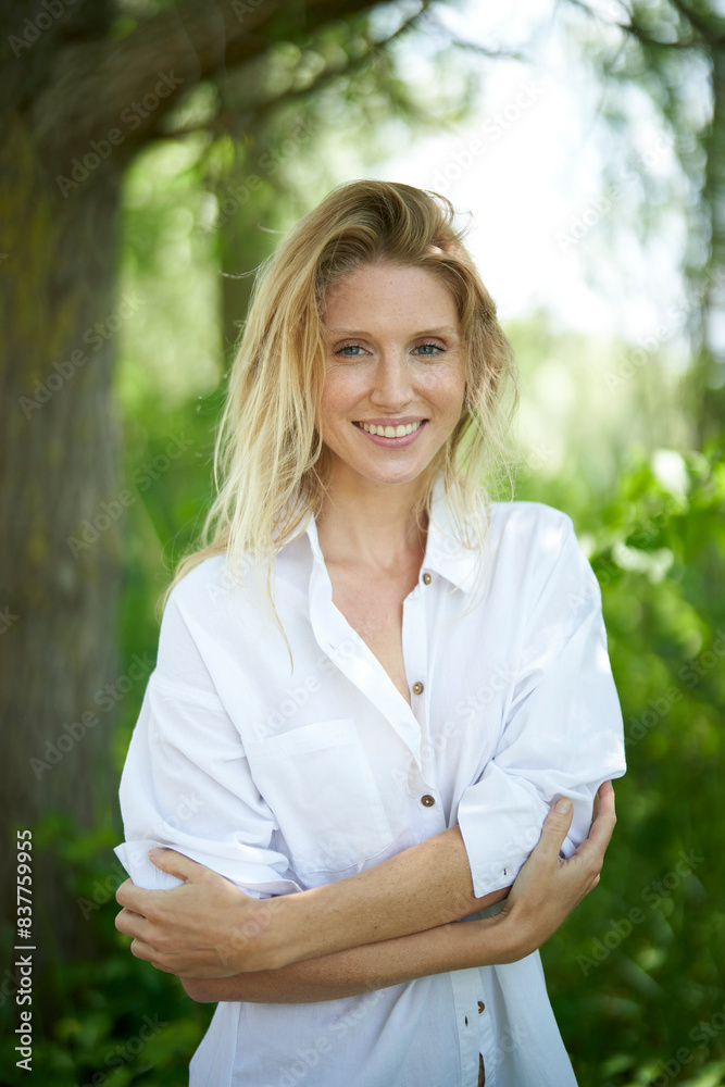 Smiling woman wearing white shirt and arms crossed standing in forest Smiling woman wearing white shirt and arms crossed standing in forest