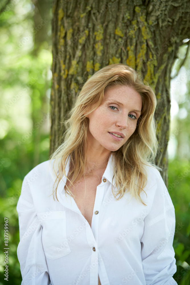 Beautiful woman in white shirt standing near tree trunk at forest Beautiful woman in white shirt standing near tree trunk at forest