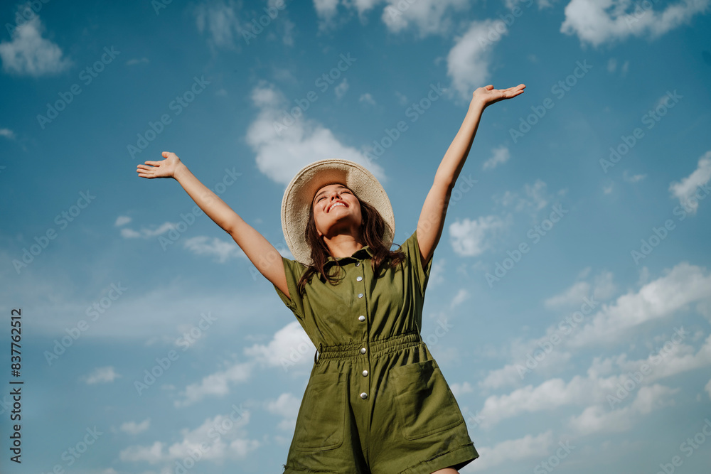 Cheerful young woman wearing green jumpsuit and hat under sky Cheerful young woman wearing green jumpsuit and hat under sky