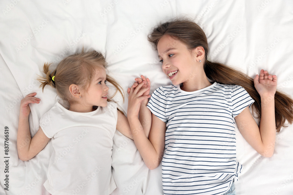 Cute little sisters on bed, top view Cute little sisters on bed, top view