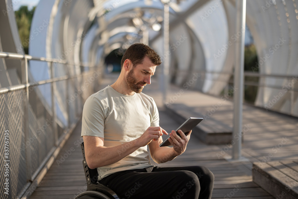 Man with disability using tablet PC sitting on wheelchair at bridge Man with disability using tablet PC sitting on wheelchair at bridge