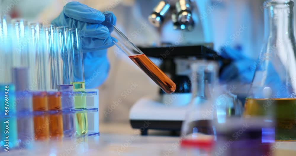 Scientist mixes chemicals in laboratory and holds test tube with orange liquid Scientist mixes chemicals in laboratory and holds test tube with orange liquid