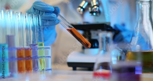 Scientist mixes chemicals in laboratory and holds test tube with orange liquid