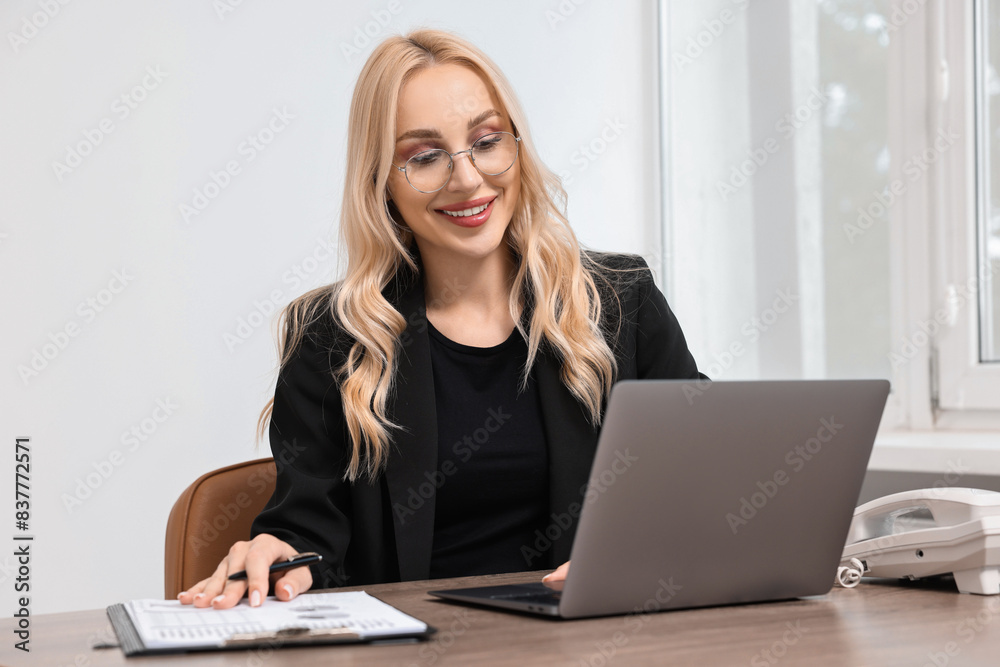 Happy secretary working with laptop at table in office Happy secretary working with laptop at table in office