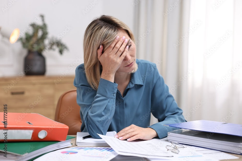 Overwhelmed woman sitting at table with documents in office Overwhelmed woman sitting at table with documents in office