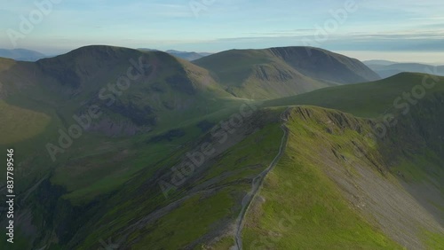 Flying above mountain path towards ancient glaciated mountains and fells during golden hour. Grisedale Pike, Lake District, Cumbria, England, UK photo
