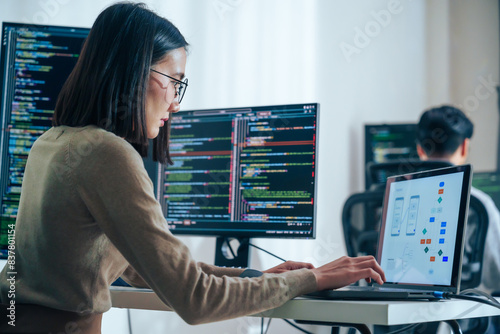 Asian software developers working on multiple screens displaying code and application diagrams in a modern office