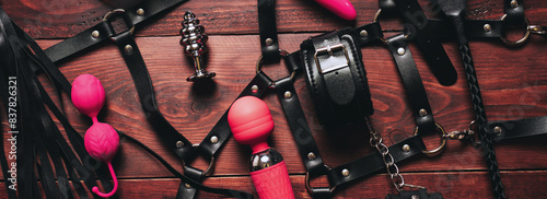 set of BDSM sex toys with handcuffs, whip flogger and vibrator for submission and female masturbation and orgasm on a wooden background. Wide header cover for sex shop