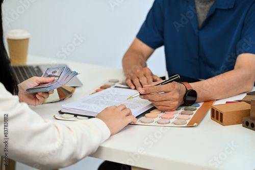 Cropped shot female client signing contract and paying cash to male contractor