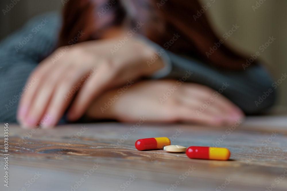 Medicinal drugs on a table with a drugged or passed out woman in the background. Concept for drug abuse or addiction. Medicinal drugs on a table with a drugged or passed out woman in the background. Concept for drug abuse or addiction.