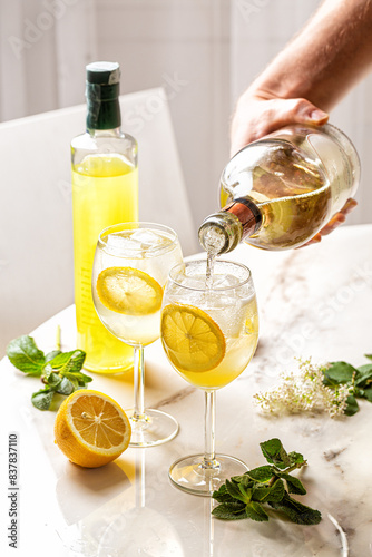 Making The Limoncello Spritz cocktail, combination of limoncello, sparkling wine and soda with lemon, ice and mint. Mans hand holding a bottle, white wine flowing. Italian summer drink.