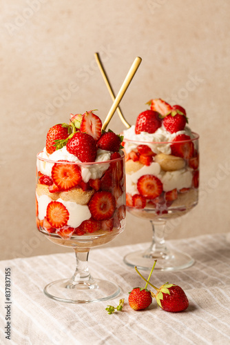 Strawberry tiramisu or trifle in two glasses. Italian dessert on a light table and beige background. Vertical image. photo