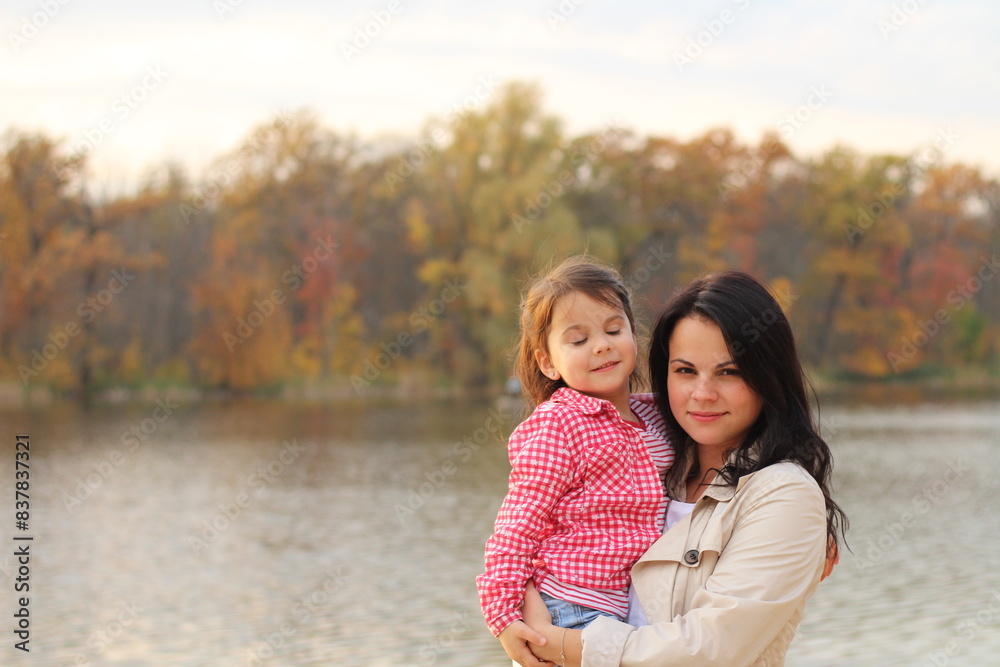 A beautiful little girl and her mother against the backdrop of an autumn pond. The concept of a family vacation in nature. Vibration of color A beautiful little girl and her mother against the backdrop of an autumn pond. The concept of a family vacation in nature. Vibration of color