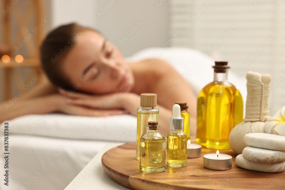 Aromatherapy. Woman relaxing on massage couch in spa salon, focus on bottles of essential oils, herbal bag, burning candle and stones Aromatherapy. Woman relaxing on massage couch in spa salon, focus on bottles of essential oils, herbal bag, burning candle and stones