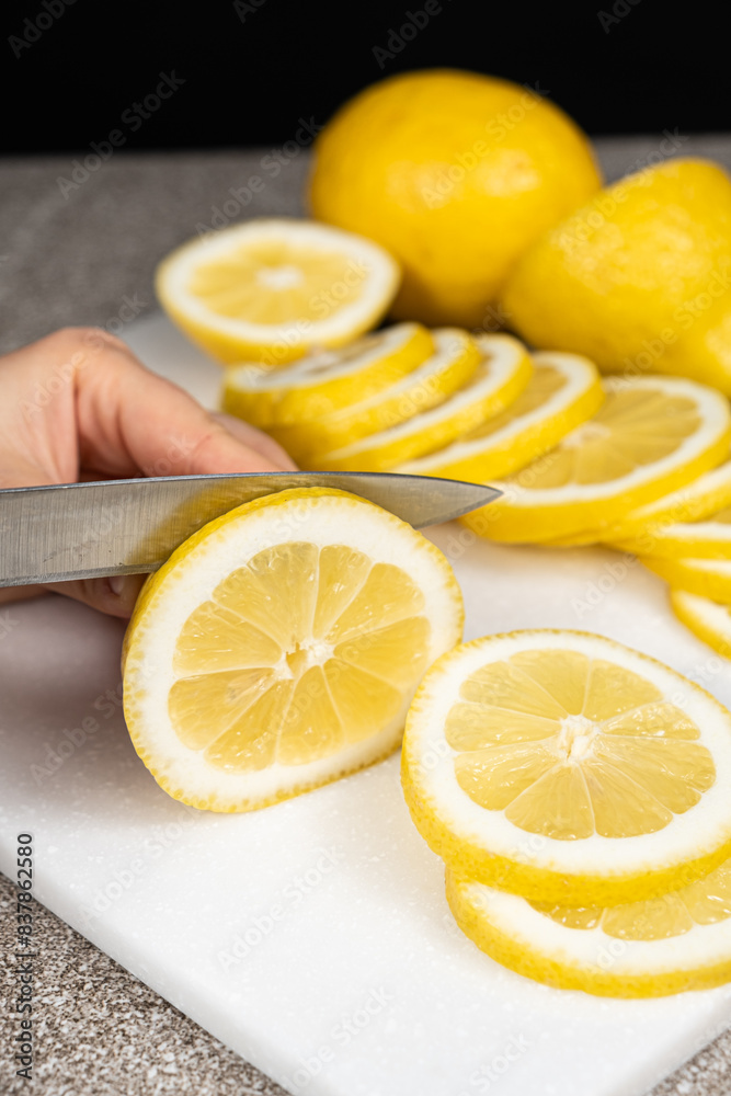 Woman cutting lemon into slices with a sharp utility knife on a stone kitchen board. Woman cutting lemon into slices with a sharp utility knife on a stone kitchen board.