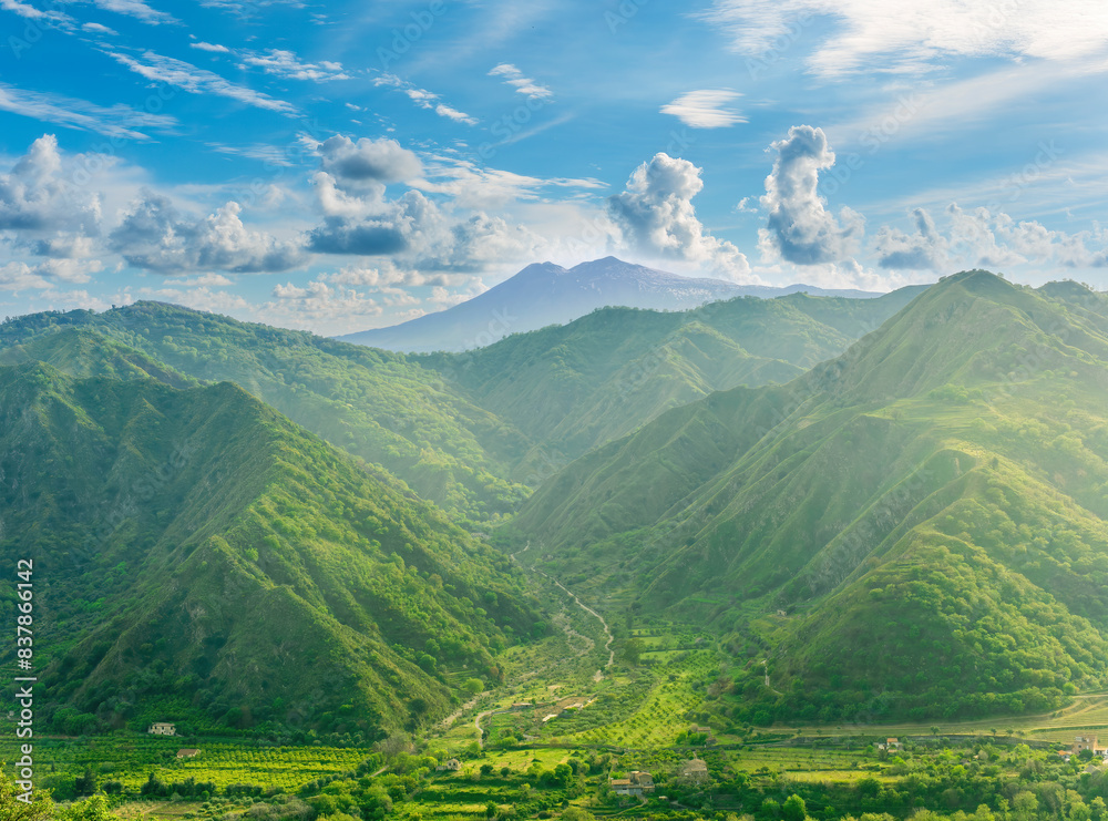 Fototapeta premium amazing view at a green landscape between two mountains with a high peak with snow and blue cloudy sky on background