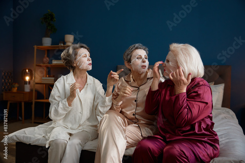 Senior women applying anti-aging cotton facial mask having fun together photo