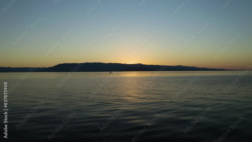 Boat In Silhouette Cruising In Distance Across Flathead Lake In Montana At Sunset In Summer. drone shot Boat In Silhouette Cruising In Distance Across Flathead Lake In Montana At Sunset In Summer. drone shot