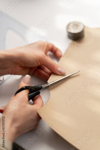 close up professional seamstress works with craft paper to cut out future patterns for a dress