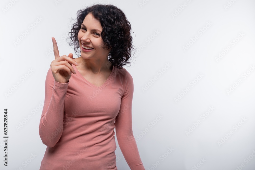 A brunette with curled hair wearing a pink blouse holds her index finger to the side A brunette with curled hair wearing a pink blouse holds her index finger to the side