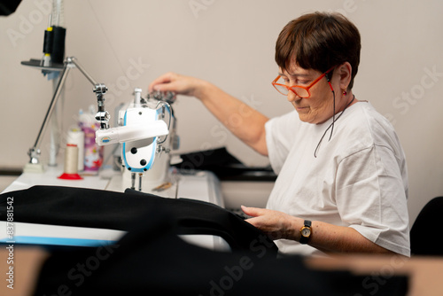 in a sewing workshop on a machine the old seamstress master makes cut on a black fabric