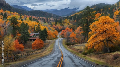 Scenic autumn road with vibrant fall foliage, winding through mountains and forests under a cloudy sky. © Sweet Mango