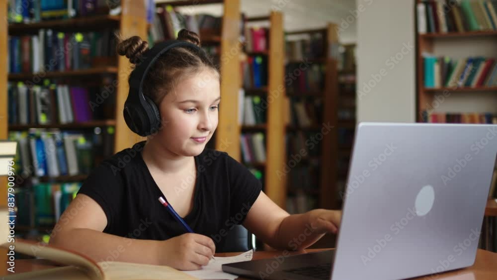 Distance learning concept. Schoolgirl studying online using laptop, taking notes on paper. Teenage schoolgirl wearing headphones undergoes online learning. Distance learning concept. Schoolgirl studying online using laptop, taking notes on paper. Teenage schoolgirl wearing headphones undergoes online learning.