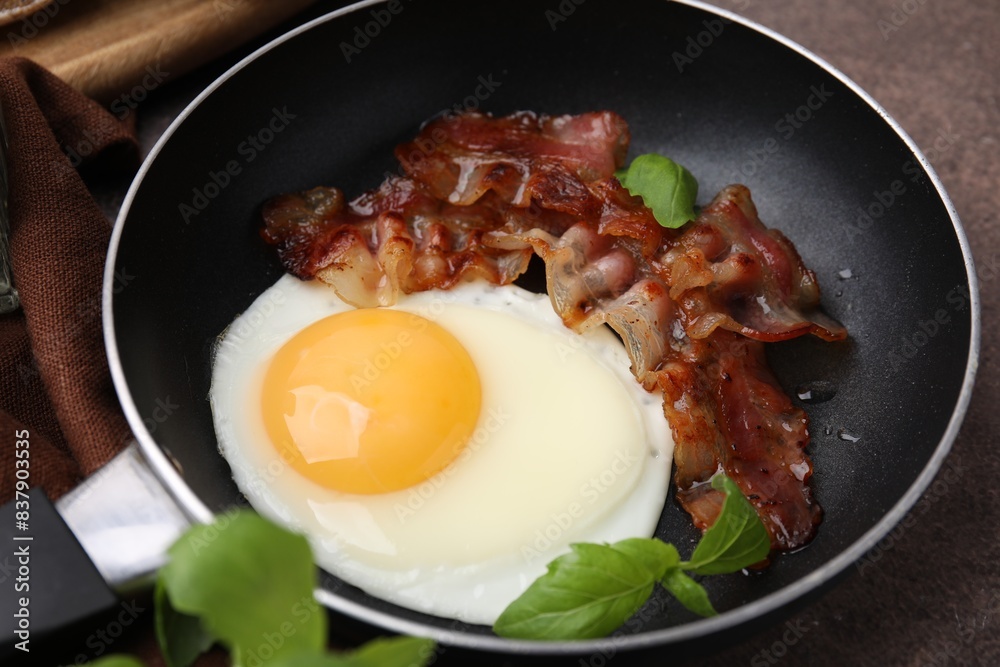 Fried egg, bacon and basil in frying pan on brown table Fried egg, bacon and basil in frying pan on brown table