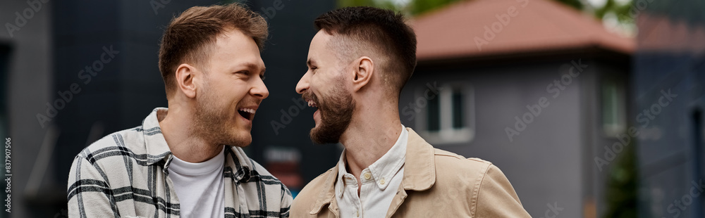 Fototapeta premium Two men in casual attire, happily standing side by side outdoors.