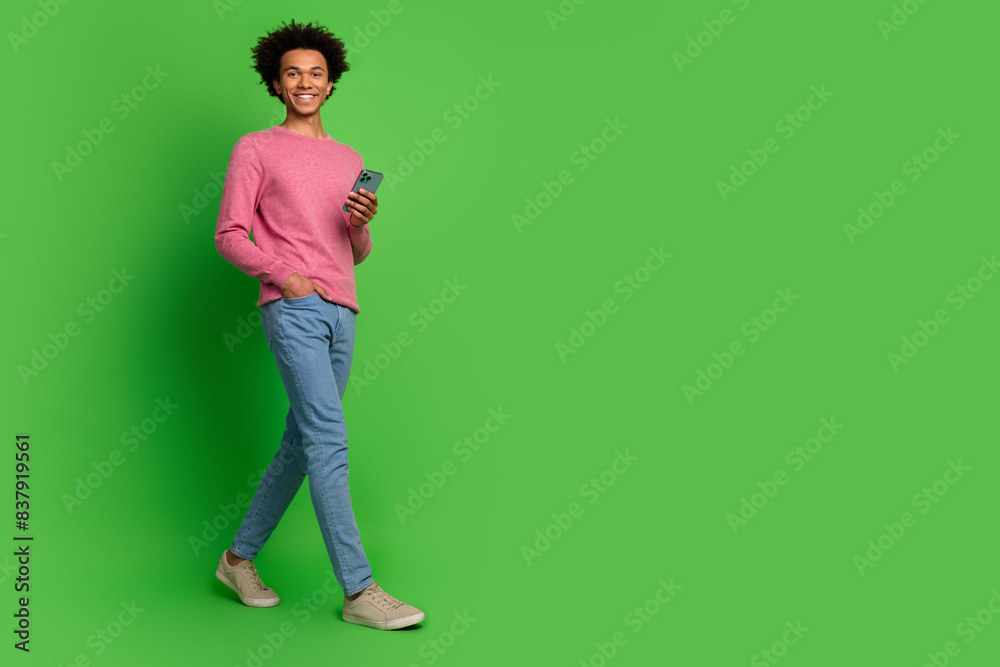 Full length photo of funky cool guy dressed pink pullover typing modern gadget walking emtpy space isolated green color background Full length photo of funky cool guy dressed pink pullover typing modern gadget walking emtpy space isolated green color background