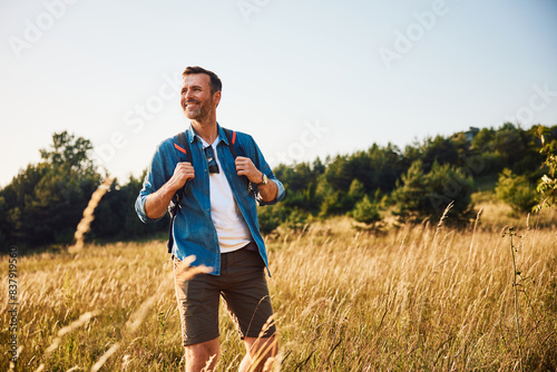 Cuadro en lienzo Handsome adult man hiking through meadow with backpack