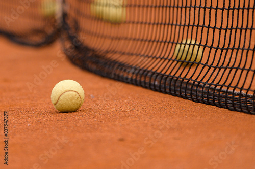 Several tennis balls on a brown court against a background of a net. One ball in focus