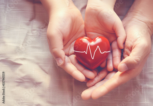 Adult and child hands holding a red heart on an aqua background symbolize heart health, donation, corporate social responsibility, World Heart Day, World Health Day, and Family Day.
