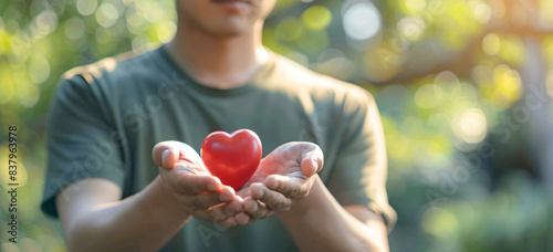 Adult and child hands holding a red heart on an aqua background symbolize heart health, donation, corporate social responsibility, World Heart Day, World Health Day, and Family Day.
