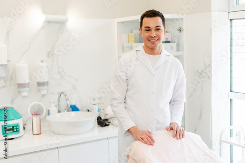 Portrait of smiling young male cosmetologist doctor in white medical uniform