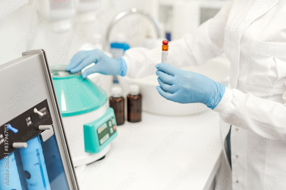 Laboratory technician, nurse or doctor holding test tube, standing in equipped medical laboratory
