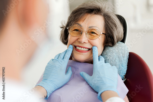 Happy senior woman sitting in dental chair, dentist looking at teeth after treatment, whitening photo