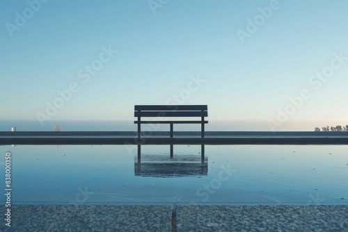 A solitary bench by a calm water body reflecting the clear blue sky  creating a serene and tranquil atmosphere.