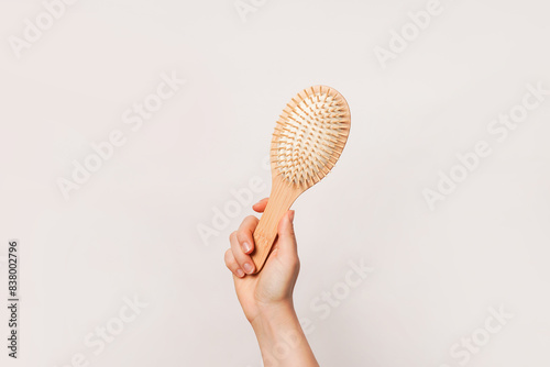 A hand is holding a wooden hairbrush against a plain background